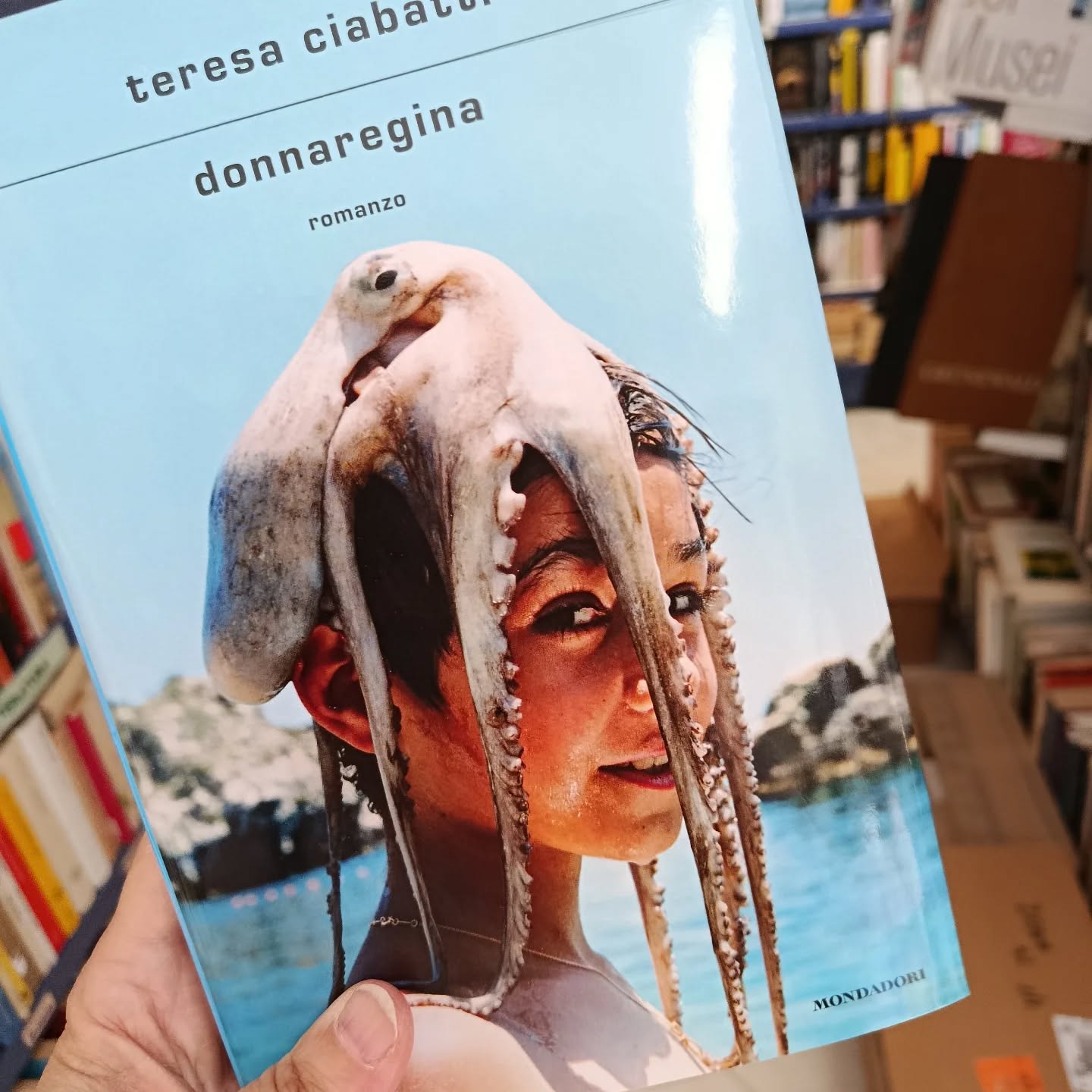 "Donna regina"
di Teresa Ciabatti
Mondadori editore
Finalista Premio Strega 2026
Chi è davvero 'o Nasone, accusato di rapina a mano armata, associazione a delinquere, associazione mafiosa, 182 omicidi commessi e commissionati? Se lo chiede la scrittrice a cui il giornale dà l'incarico di intervistare proprio lui, il superboss. A lei che di criminalità non sa niente, che si è sempre occupata di adolescenti, tutt'al più cantanti, attrici, gente dello spettacolo. Il loro è l'incontro di due mondi lontanissimi che tali devono rimanere, almeno nelle intenzioni della protagonista.
Eppure, quando lui inizia a parlare, qualcosa cambia. Quest'uomo spietato che alleva colombi e crede negli ufo comincia a interessarla. Non tanto quando si sofferma sulle cronache di furti, sparatorie e vendette, piuttosto per la nostalgia che vibra nei racconti delle donne incontrate e perdute, degli amici morti ammazzati, degli affetti famigliari. Quando insomma, pur non rinnegando il proprio passato, il boss si mostra vulnerabile. Il dubbio: forse la sta manipolando? È sul piano dei rapporti affettivi che i due si incontrano: nelle ferite di genitori incerti, forse sbagliati. Nel mistero dei figli con cui non sanno più comunicare e che temono di aver perso per sempre. Il confronto tra loro, pur sempre carico di diffidenza, si trasforma allora in un viaggio tra ricordi, confessioni, fraintendimenti e proiezioni, ma soprattutto rivelazioni su figli che non sono quello che loro credono. Così, quando la protagonista si trova a cercare le tracce del figlio del boss nelle strade di Napoli, capisce di cercare qualcun altro: sua figlia che le sta sfuggendo.
#teresaciabatti #donnaregina #mondadorieditore #finalistapremiostrega2026